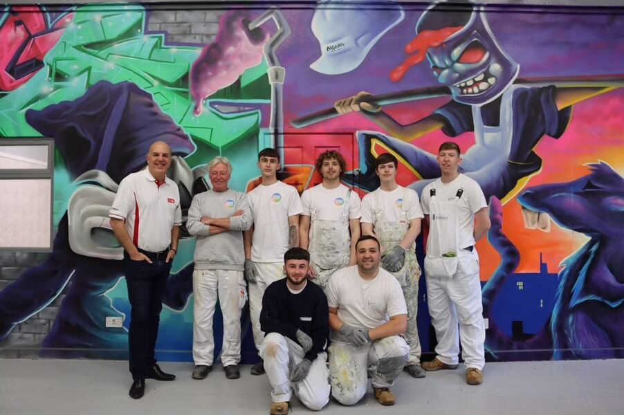 Eight People Stand In Front Of A Large Graffiti-Style Mural Dedicated To Bagnalls