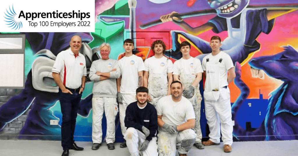 Eight People Stand In Front Of A Large Graffiti-Style Mural Dedicated To Bagnalls. The Apprenticeships Top 100 Employers 2022 Logo Is In The Top Left Corner