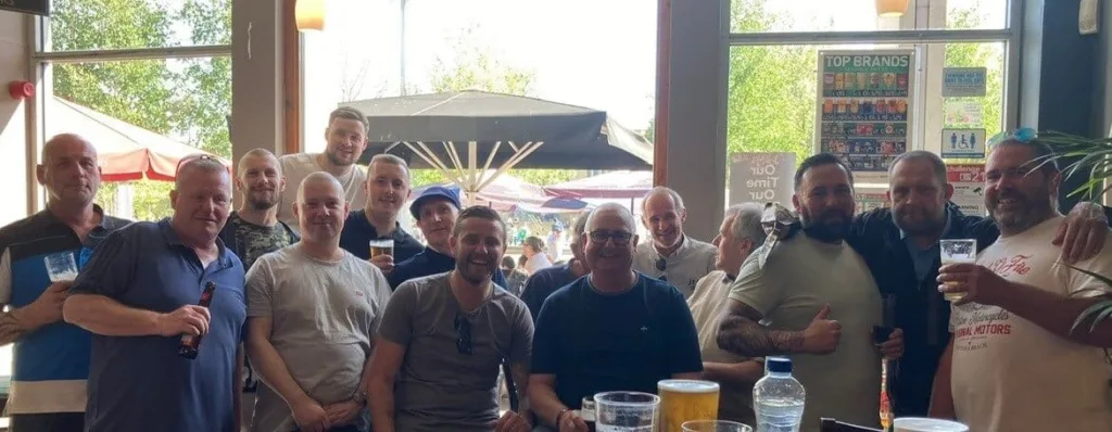 Fifteen People Stand Together In A Pub Holding Drinks And Smiling