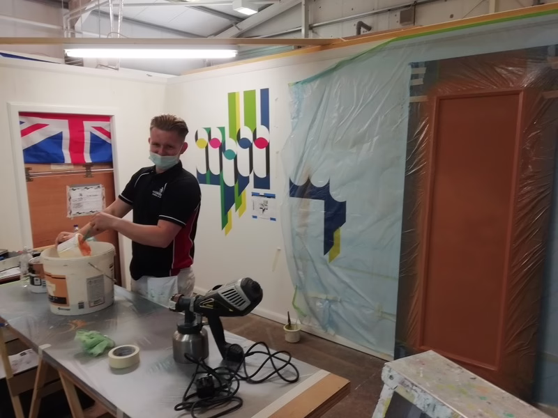 Lewis Boyle Preparing Paint In Front Of His Brightly Coloured Wall Mural