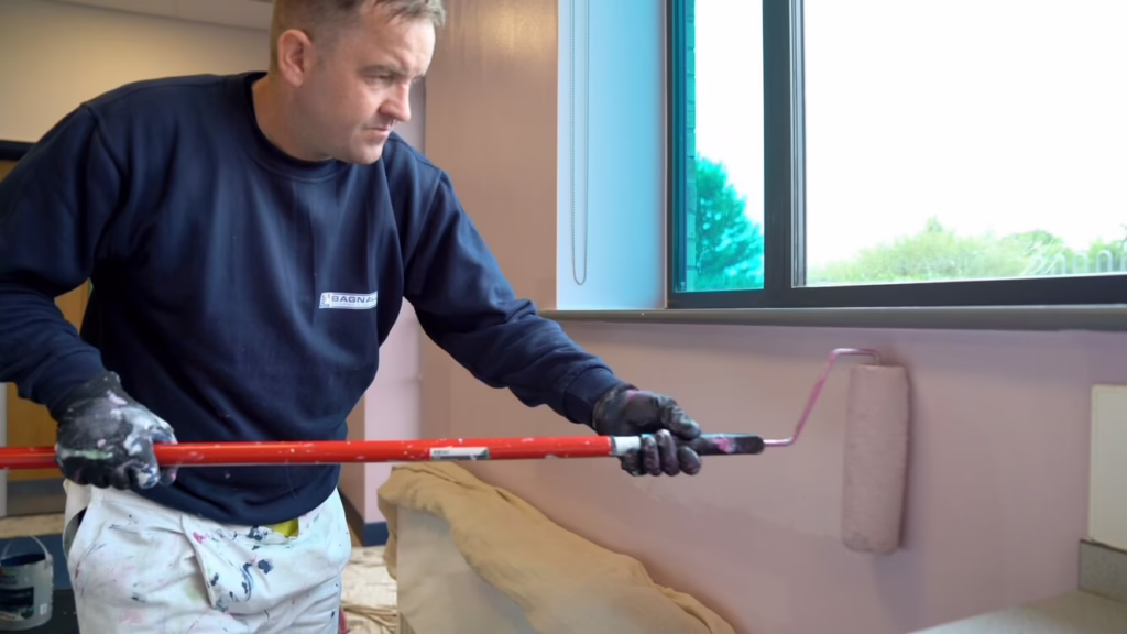 A Man Painting A Wall With A Paint Roller