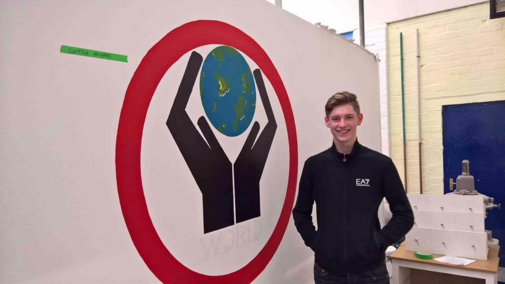 A Young Man Stands Next To A Painted Sign That Depicts A Pair Of Hands Holding A Globe