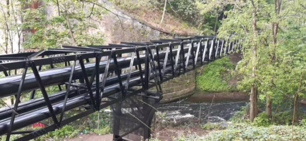 Metal Pipework Suspended Above A River At Riverside In Preston