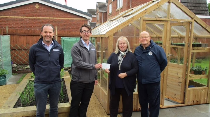 Four People Stand In Front Of A Greenhouse Full Of Plants