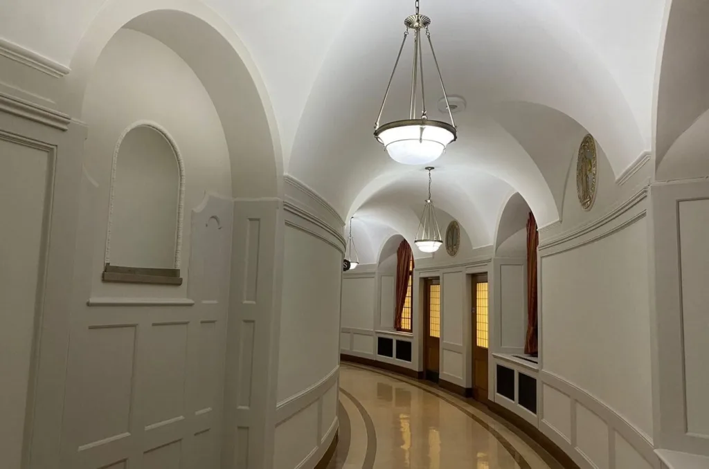 A Curved Corridor Painted White With Hanging Light Fixtures